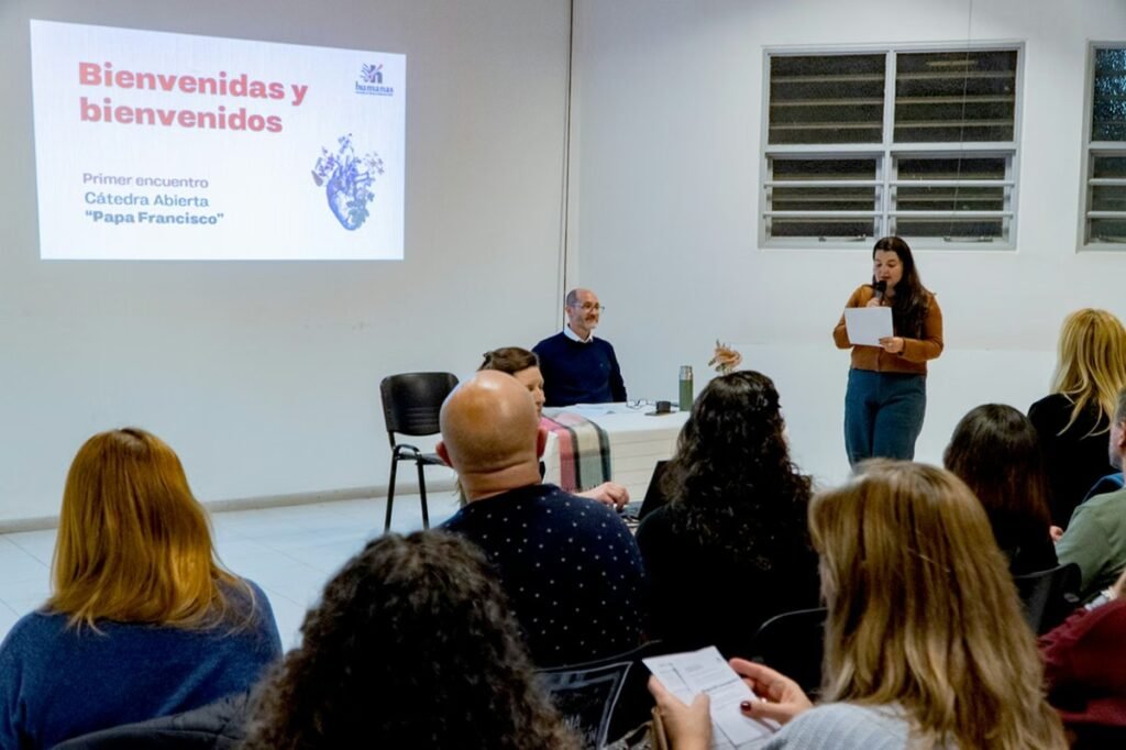 La imagen muestra a una mujer en medio de una disertación, frente a la mirada atenta del decano de la Factultad de Ciencias Humanas de la Universidad nacional de Río Cuarto, Cristian Santos, en el marco de la cátedra abierta Papa Francisco.